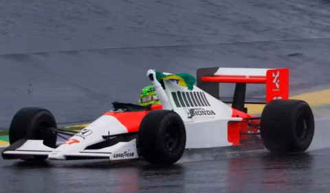 Pilotando carro de Ayrton Senna, Lewis Hamilton dá volta com a bandeira do Brasil em mãos