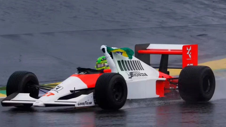 Pilotando carro de Ayrton Senna, Lewis Hamilton dá volta com a bandeira do Brasil em mãos